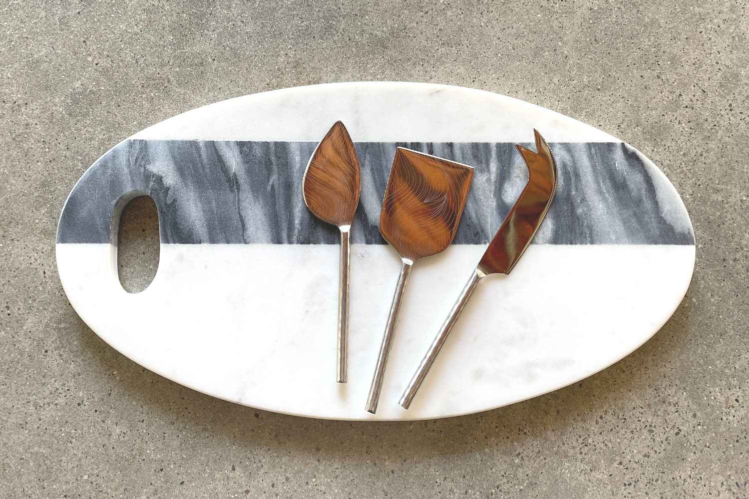 white and gray oval charcuterie tray with stainless knife, spatula, and fork.