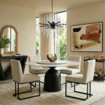 Modern round dining table with black pedestal base surrounded by cream boucle chairs on neutral wool rug with black crystal chandelier overhead.